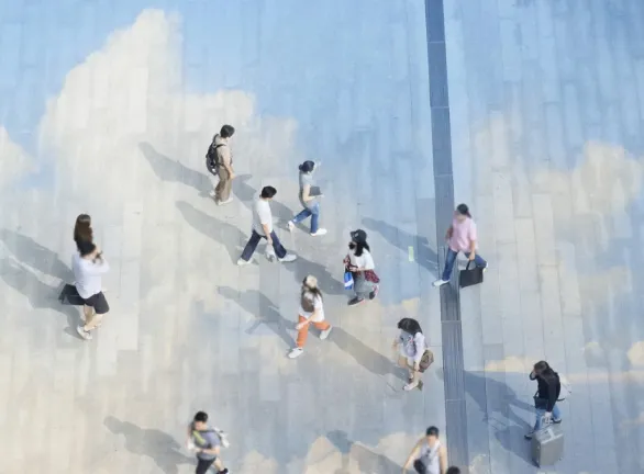 People walking on a building with painted clouds.