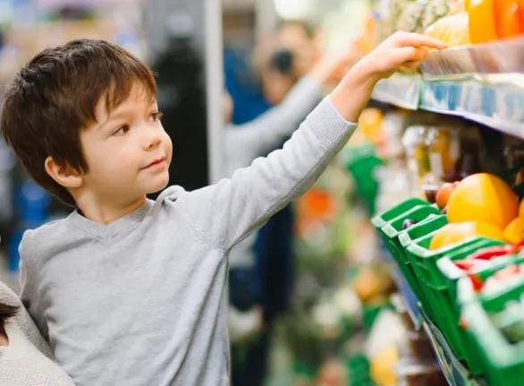 A woman and child browsing vegetables in a supermarket, carefully inspecting the fresh produce on display.